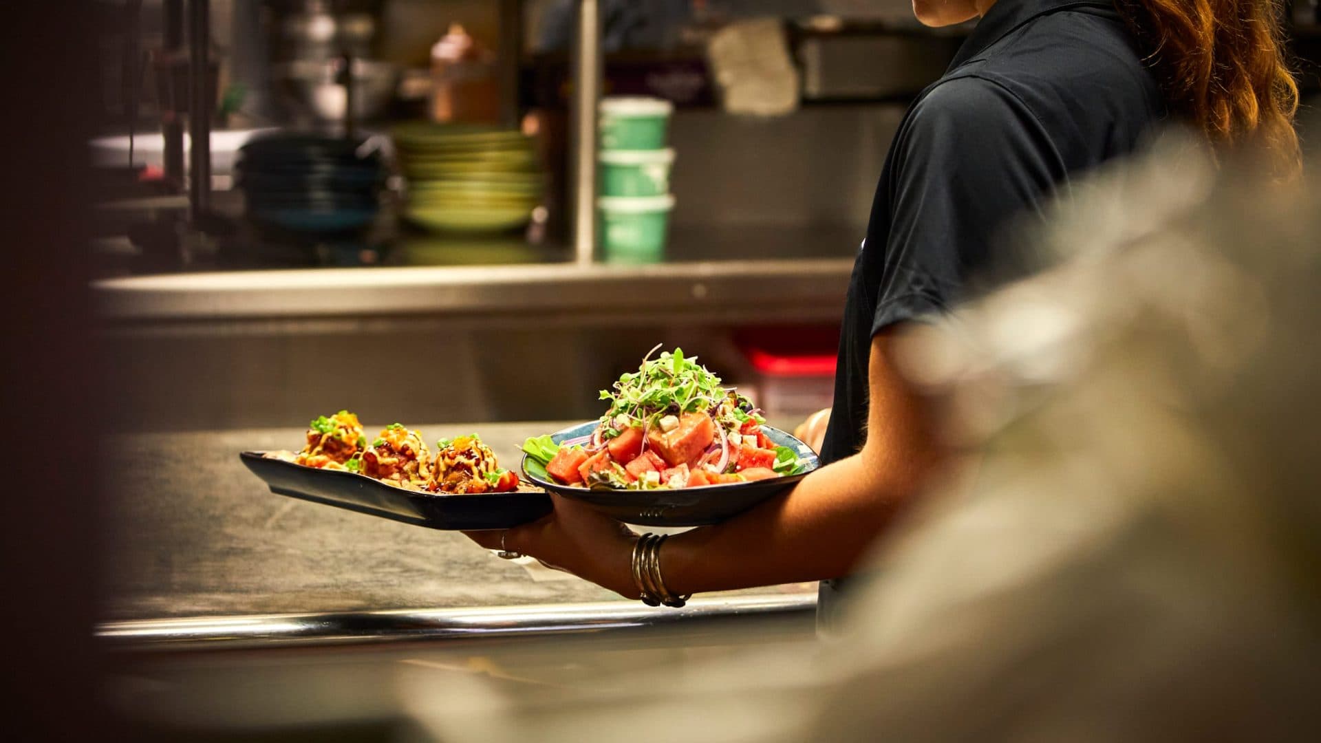 A photo of food being plated and picked up in Tiki's Grill & Bar's scratch kitchen, showcasing the fresh, prepared food.