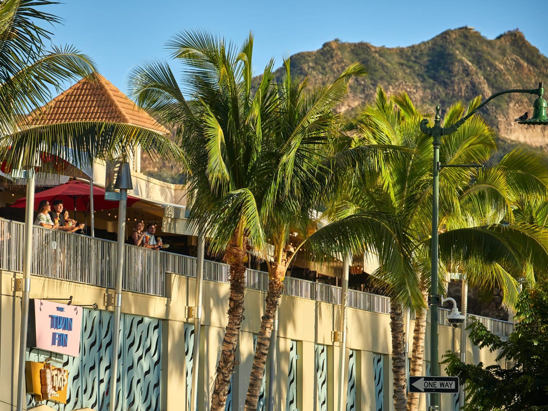 A view of Tiki's Grill & Bar's iconic open-air lanai, with guests enjoying the outdoors and Diamond Head visible in the background. A view of Tiki's Grill & Bar's iconic open-air lanai, with guests enjoying the outdoors and Diamond Head visible in the background.